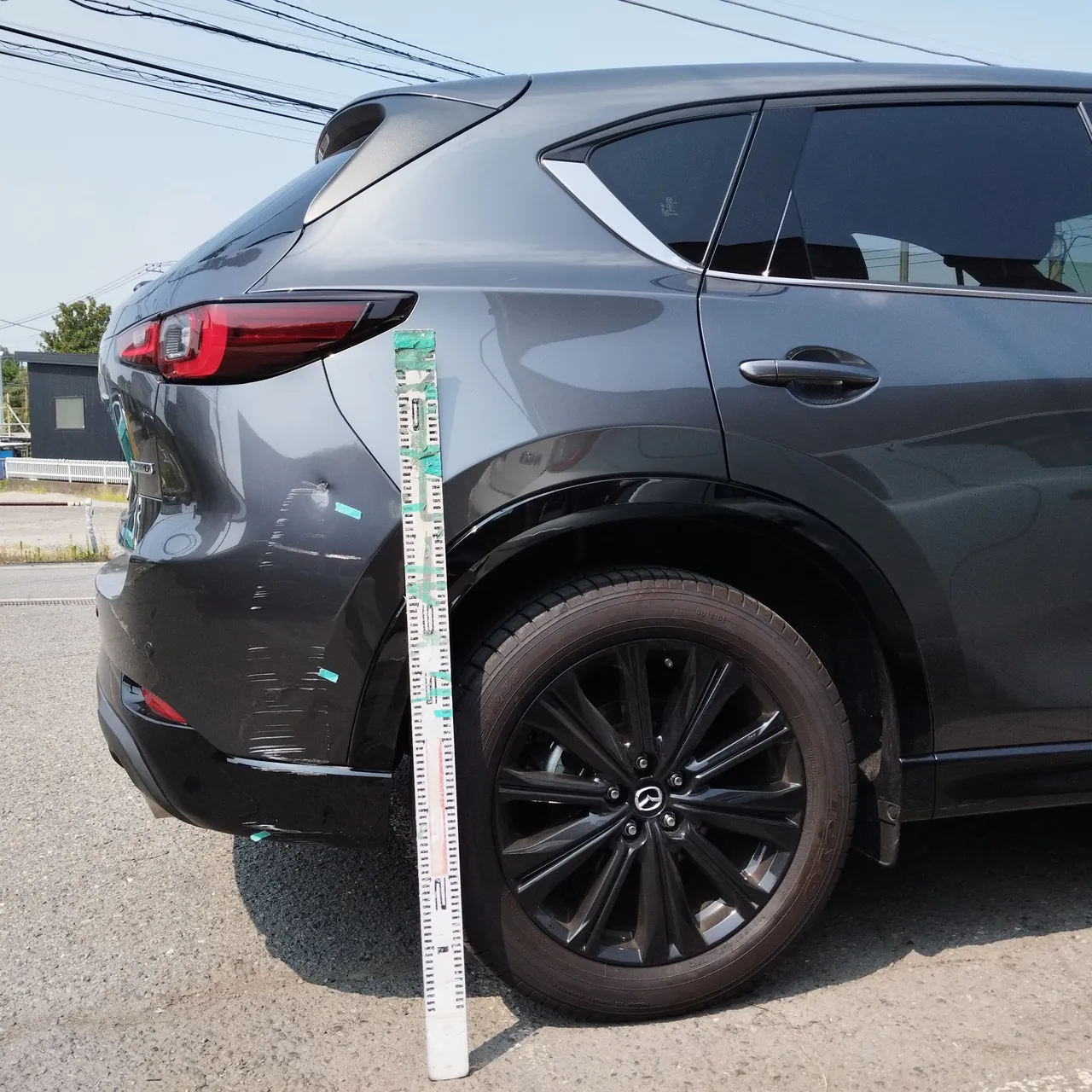 マツダ CX-5 リヤバンパー右角の擦り傷と打痕。目盛りの棒を立てて撮影