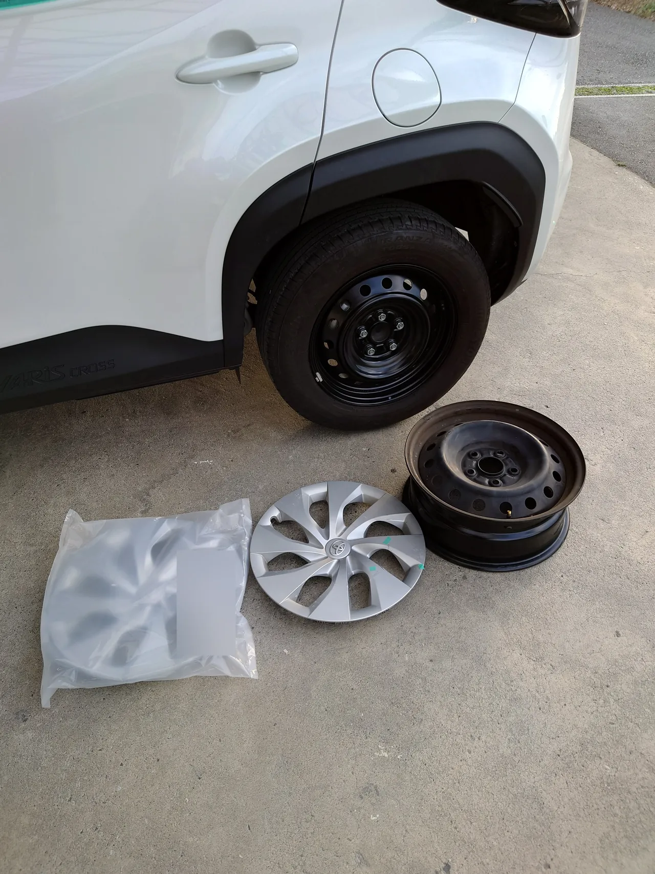 新しいディスクホイールを付けたヤリスクロスの左リヤ。床に袋入りの新しいホイールキャップと外した元のホイール