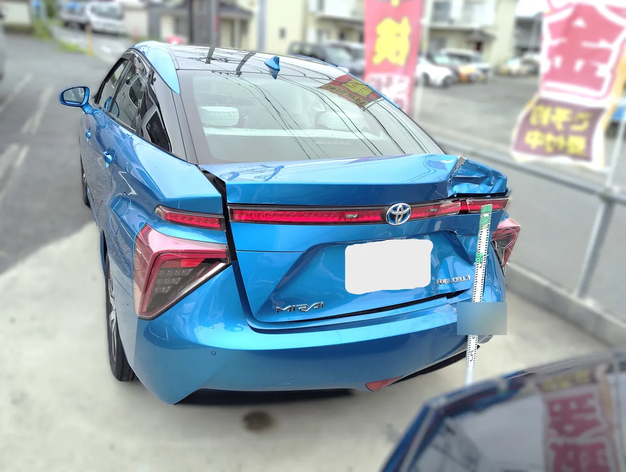 トヨタ MIRAI(ミライ)の修理前の後ろ(左斜め後ろから)。トランクの右半分がつぶれて持ち上がり、右テールランプのまわりも傷んでいる