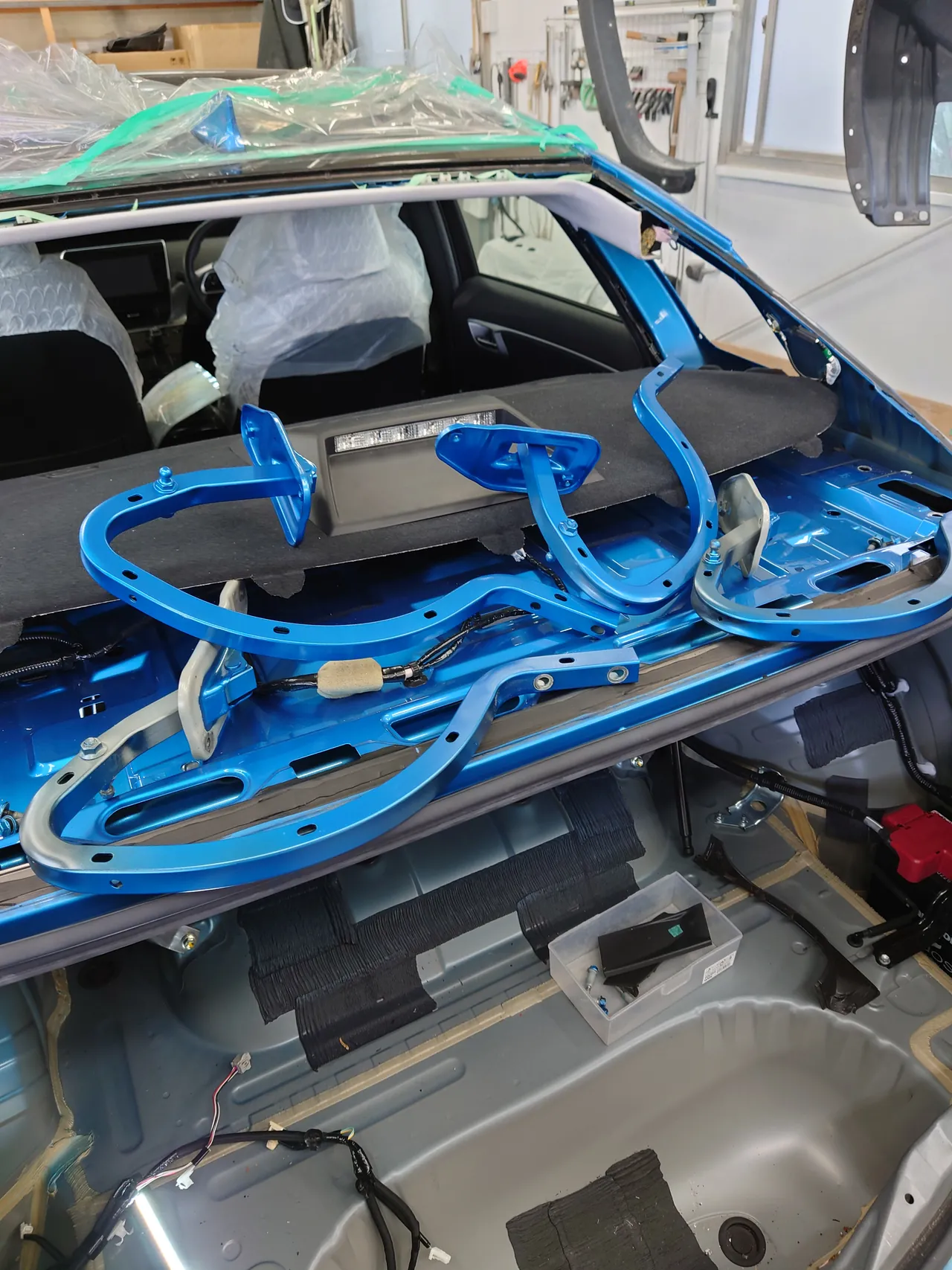 リヤガラスとトランクを外したMIRAIの後ろ。窓の開口部から車内の座席が見え、外した青いトランクのヒンジが棚の上に置いてある