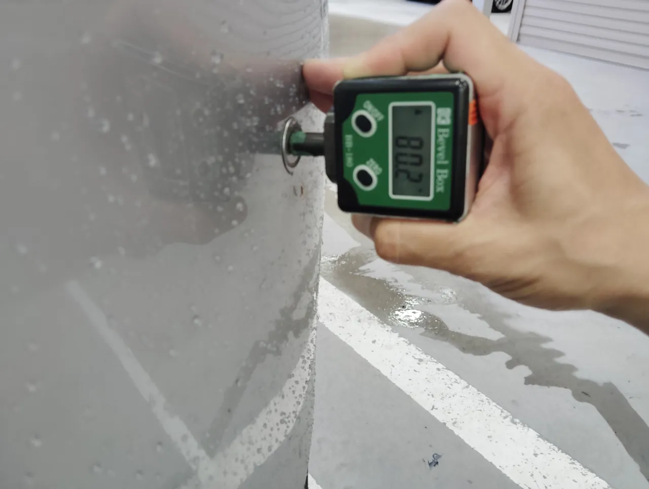 プリウスの車体の丸い部品にデジタル式の角度計の軸を当て、角度を表示しているところ（修理後）