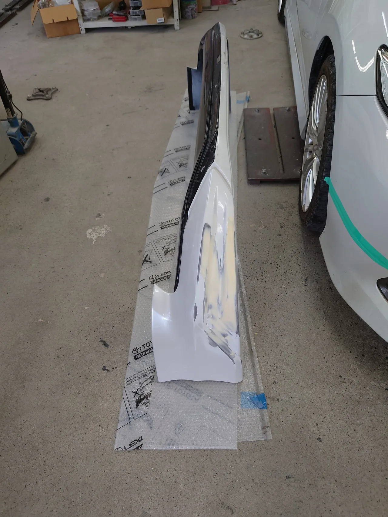 床のシートに置いたカムリのフロントスポイラー全体。手前の右端にクリーム色のパテ