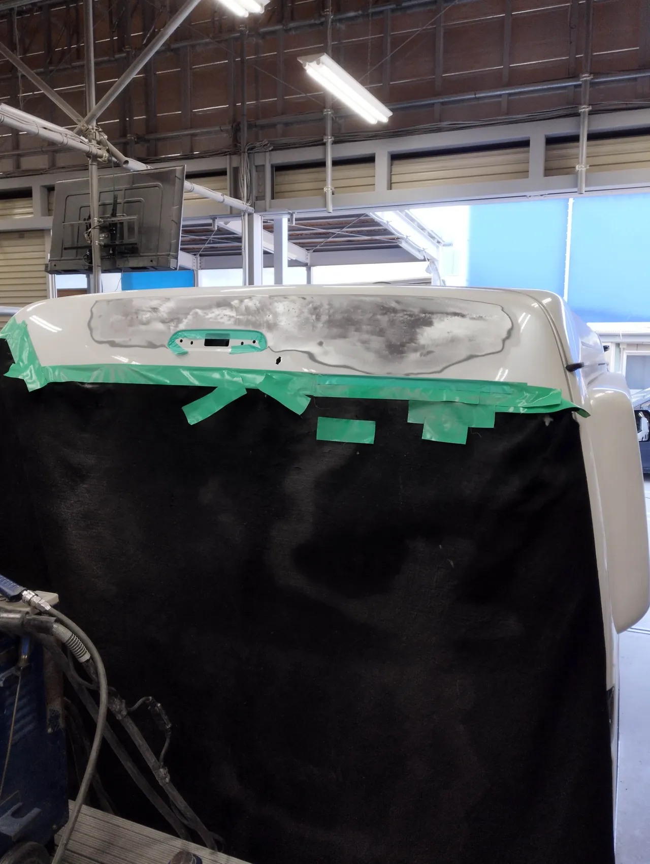 ハイエースのバックドア上部を研いで鉄板を出したところ。くぼみの部品を外し、ガラスから下を黒い布で覆う