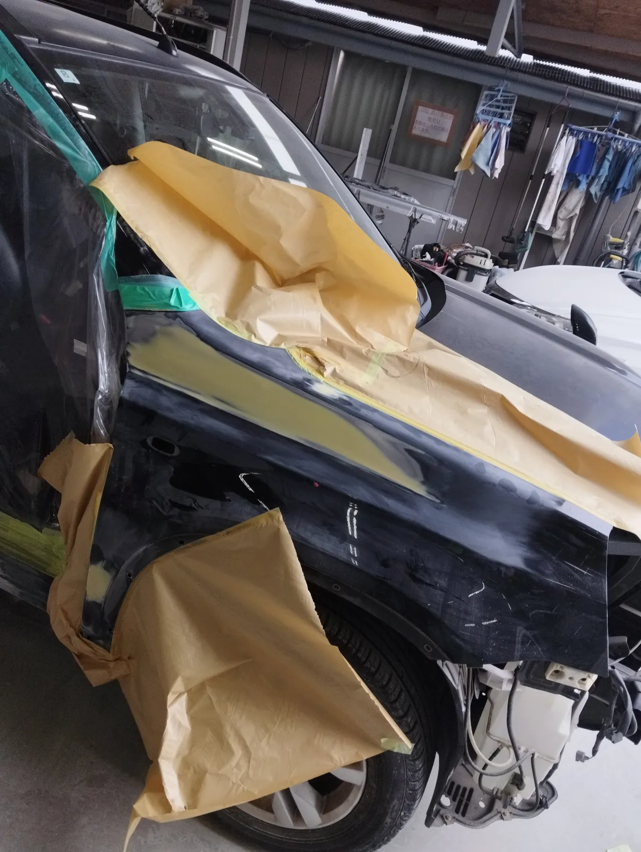 日産 T31エクストレイルの右フロントフェンダー。上の帯のパテを研ぎ、まわりを紙で囲んだところ（フロントバンパーは外してある）