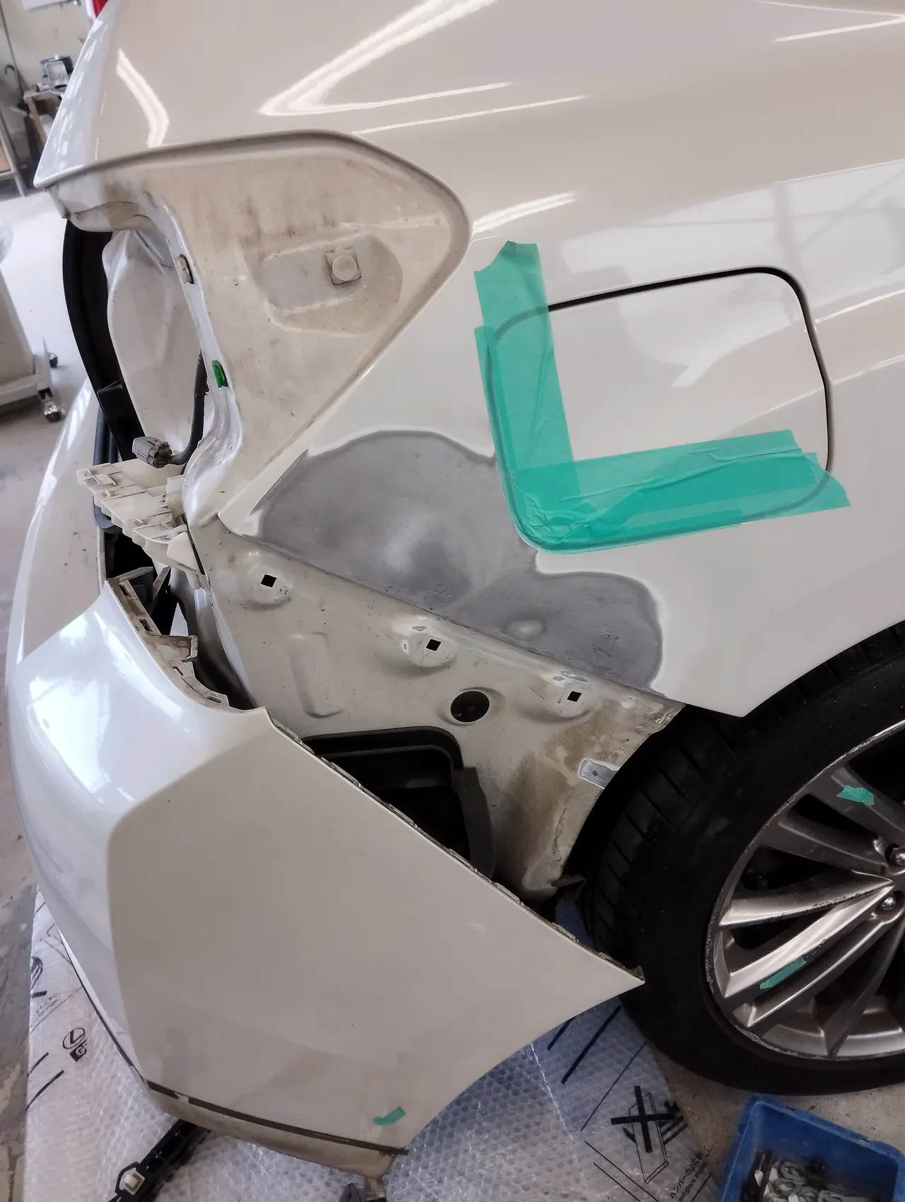 引き出したあとのインプレッサの右リヤクォーターの下。研いで鉄板が出た面と、緑のテープのL字の印