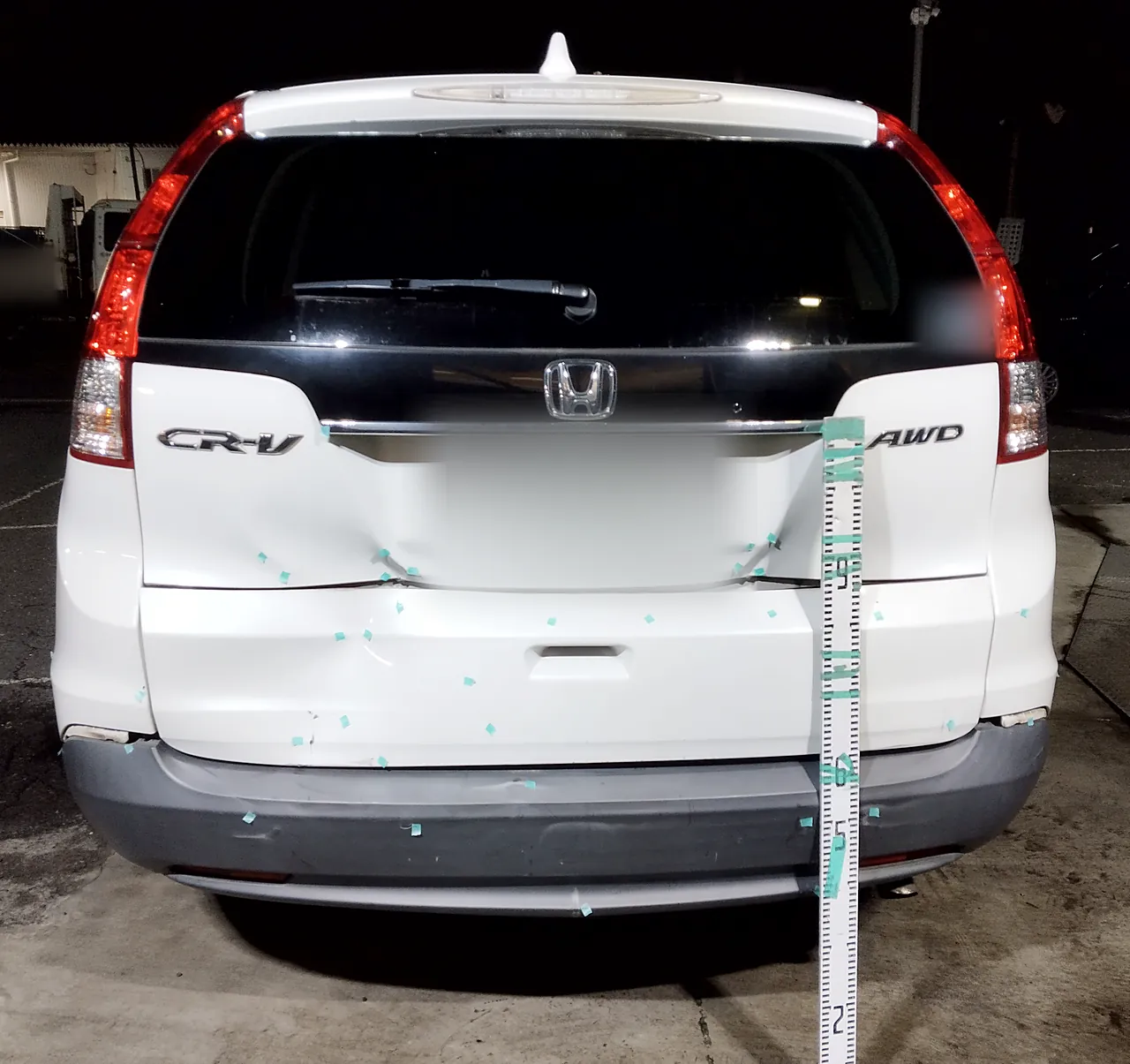 修理前のホンダ CR-V を真後ろから。バックドアの下側と、その下の白い板がへこみ、緑のテープの印と目盛りの棒