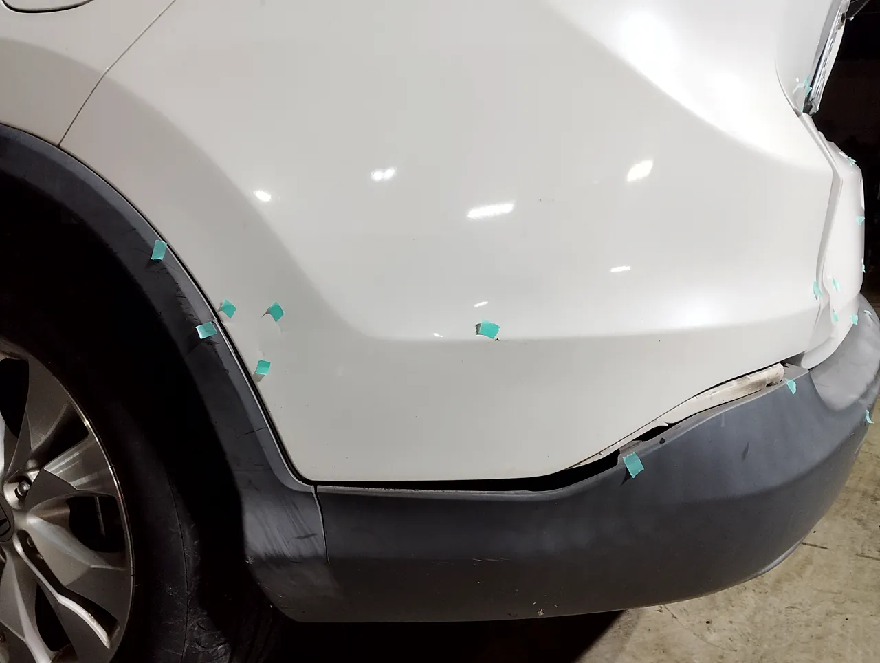 修理前のホンダ CR-V の左の後ろの角。バンパーの白い角と下の黒い部分のあいだにすき間（緑のテープの印）