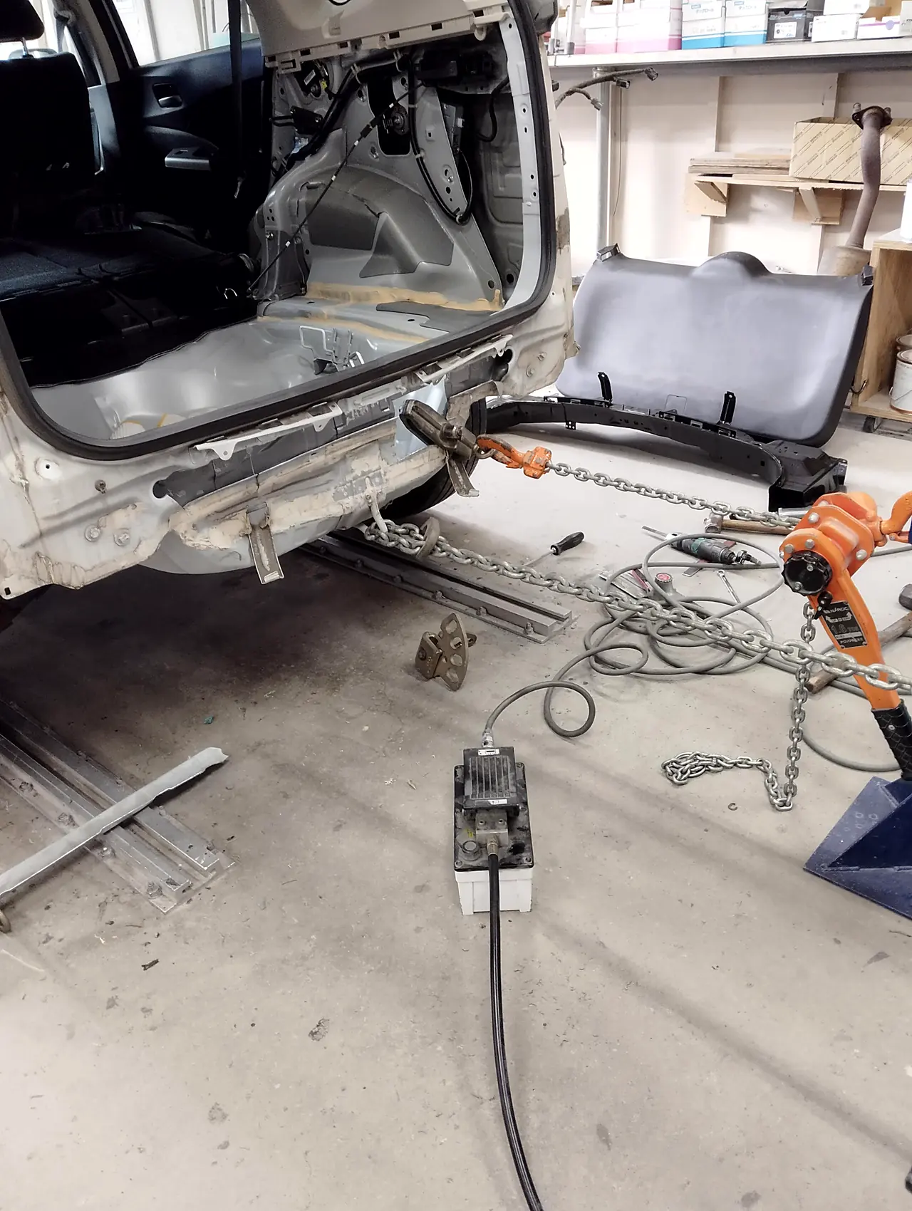 バンパーとバックドアを外したホンダ CR-V の後ろの端をクランプでつかみ、チェーンとオレンジの巻き上げ機で後ろへ引く
