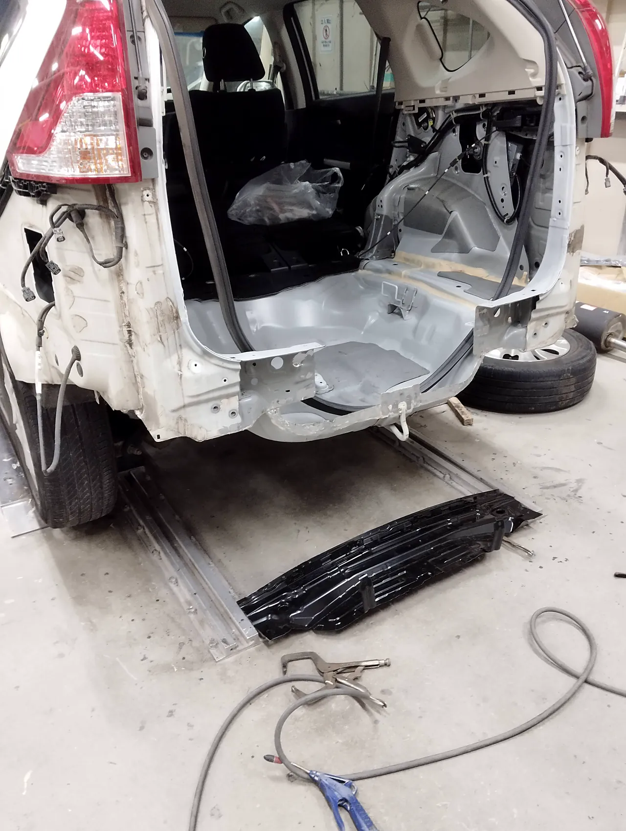 古いバックパネルを外したホンダ CR-V の後ろの開口部と、床に置いた新しいバックパネル（まだ車の色が塗られていない下地の状態）