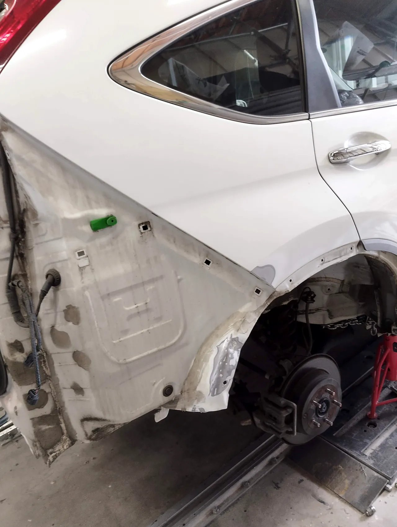 ホンダ CR-V の右リヤクォーターの後ろ下の角。研いで鉄板を出した跡と、アーチの縁の薄いパテ（後輪は外してある）