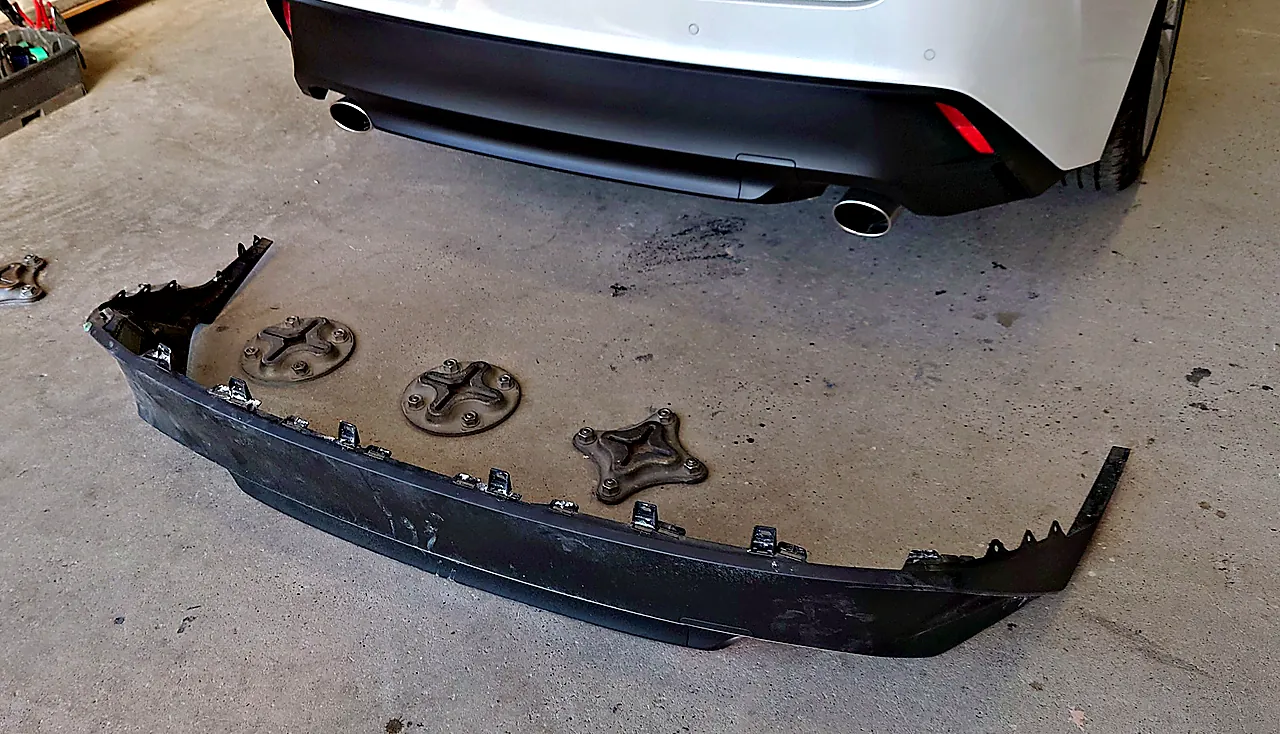 組み付けを終えたレクサスIS 300hの後ろの下側。車には汚れのない黒い下側の部品、床には外した元の部品