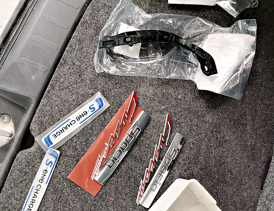 スペーシア カスタムに付ける新しいエンブレム2つ（Spacia Custom・S-ene CHARGE）と、外した元のエンブレム、袋に入った新しい取付け部品