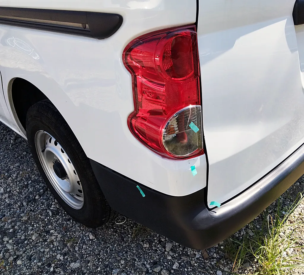 修理前のNV200バネット バンの左後ろの角。テールランプの透明な部分、その下の角、リヤバンパーの角に緑のテープの印