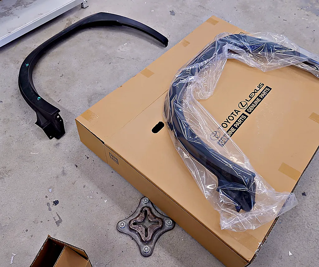レクサスUX250hから外した元のホイールアーチモール（緑のテープ付き）と、GENUINE PARTS と刷られた箱の上の袋入りの新しいモール