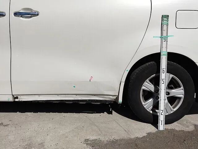 お預かりした車の側面の損傷を、計測しながら確認しているところ