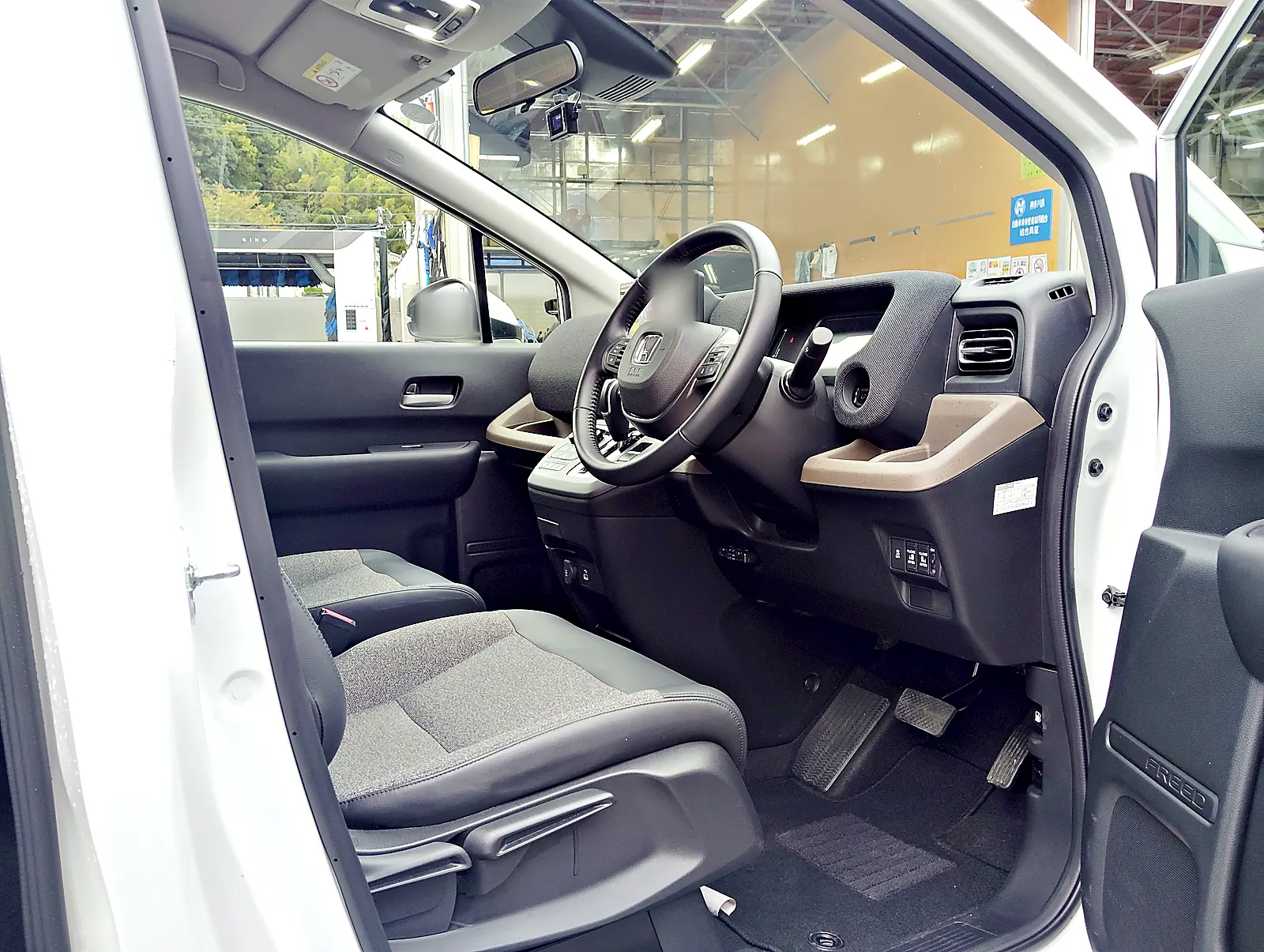 パールホワイトのフリード e:HEV の運転席。グレーと薄いベージュのダッシュボードと、座る面が布のシート