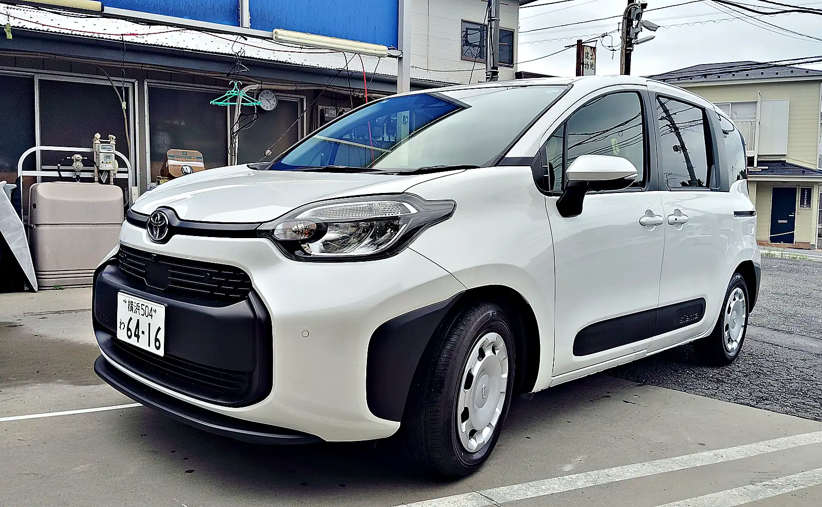 パールホワイトのシエンタ ハイブリッド G を左前の斜めから見たところ。黒い樹脂のバンパーと、キャップを付けたホイール